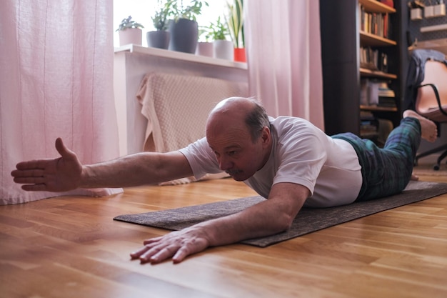 운동 매트에 Shalabhasana 변형을 하 고 수석 남자.