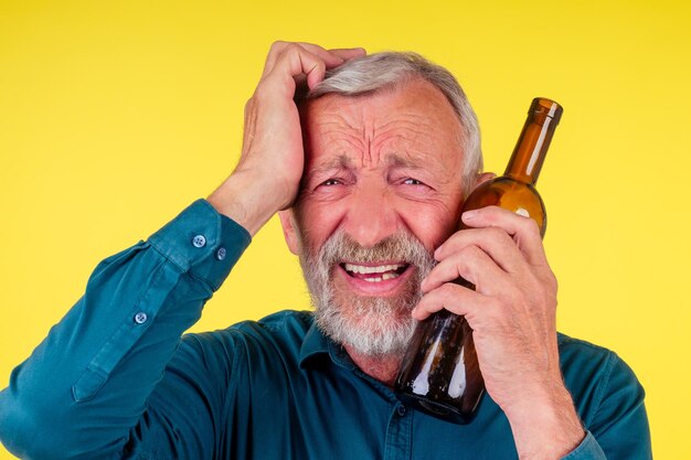 Senior man drinking alcohol alone studio yellow baclground.