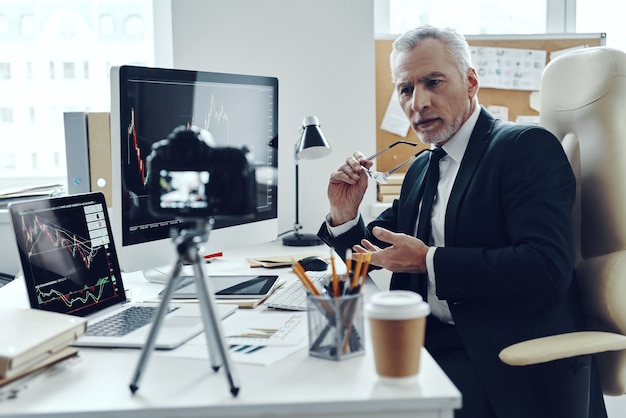 Senior man in elegant business suit using modern technologies while making social media video