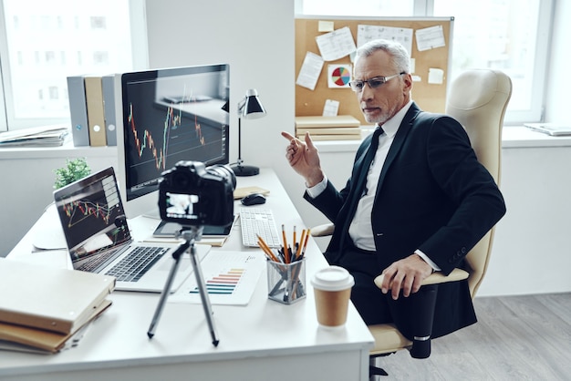 Foto uomo anziano in elegante tailleur che utilizza tecnologie moderne mentre realizza video sui social media