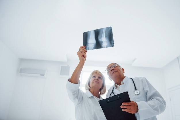 Senior man en vrouw artsen in wit uniform onderzoekt röntgenfoto's van menselijke benen.