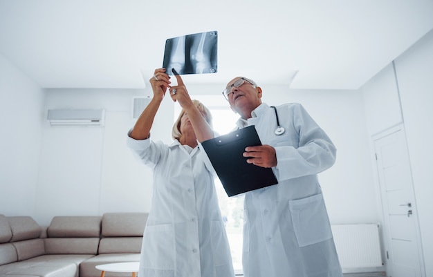 Senior man en vrouw artsen in wit uniform onderzoekt röntgenfoto's van menselijke benen.