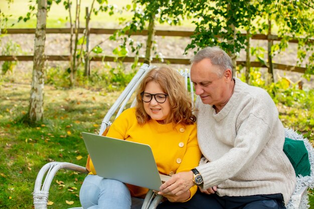 Senior man en vrouw zitten in fauteuils en met behulp van laptop in een tuin