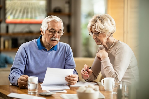 Foto senior man en zijn vrouw analyseren hun spaargeld terwijl ze thuis financiële rapporten lezen