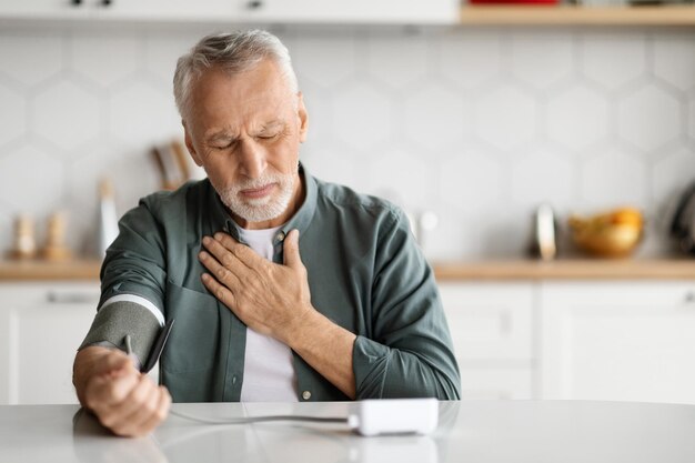 Senior man feeling unwell at home checking blood pressure with arm monitor