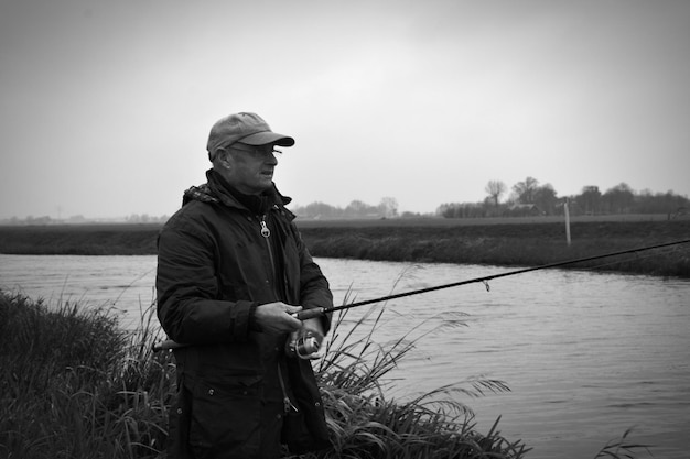Пожилой мужчина ловит рыбу в озере на чистом небе.