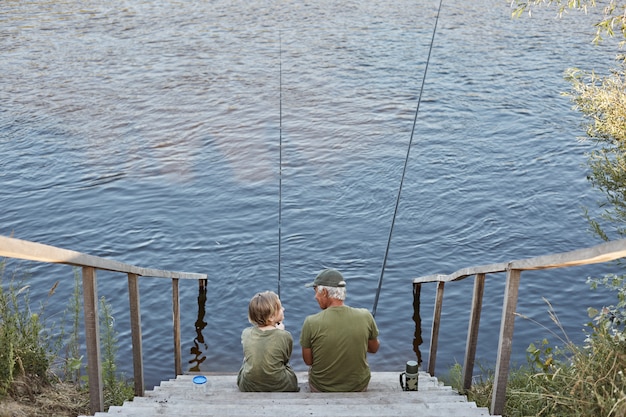 Senior man fishing with grandson, spending time near river