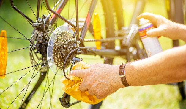 年配の男性の手がスプレーと雑巾で自転車を掃除し、自転車のスポーツコンセプトのメンテナンスを行っています