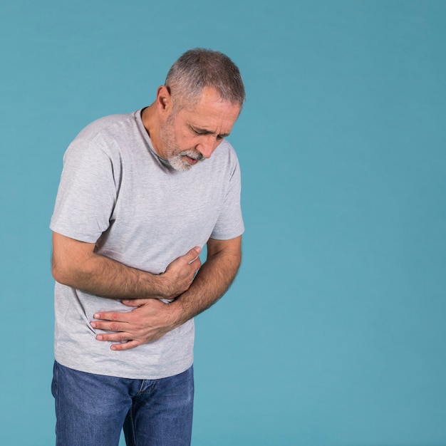 Senior man having stomach pain in front of blue backdrop