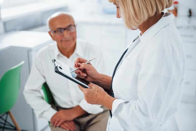 Senior man heeft overleg in de kliniek door de vrouwelijke arts.