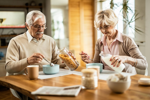 Старший мужчина и его жена завтракают хлопьями за обеденным столом
