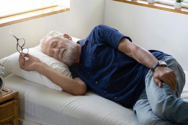 ベッドでリラックスしながら眼鏡をかぶった年配の男性