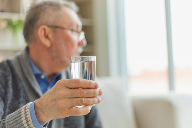 Senior man holding glass drinking fresh water at home mature old senior thirsty grandfather takes