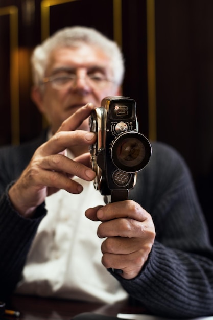 Старший мужчина держит старомодную кинокамеру.