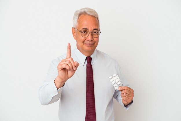 Senior man holding pills showing number one with finger.