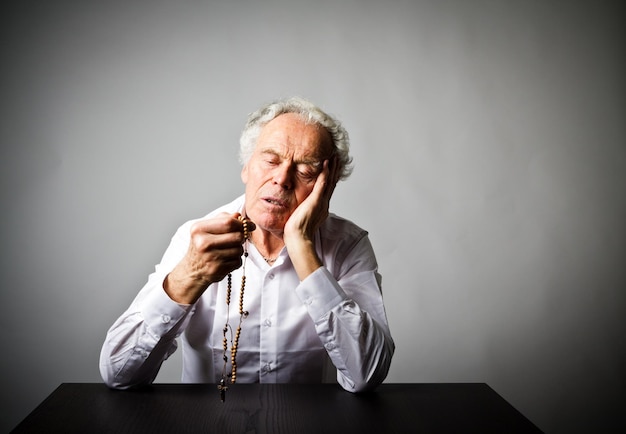 Photo senior man holding rosary beads while sitting at table against white background