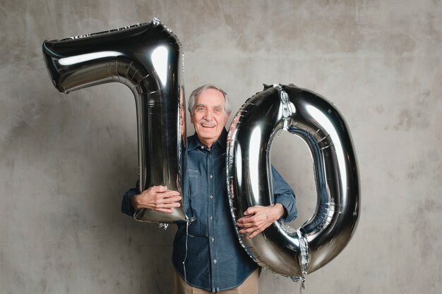 Senior man holding silver balloons for 70 years celebration