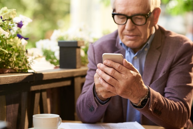 Uomo senior che tiene smartphone in caffè