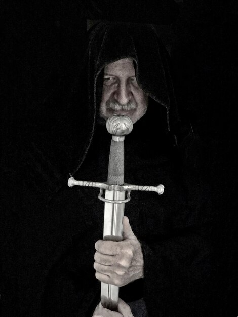 Senior man holding sword against black background