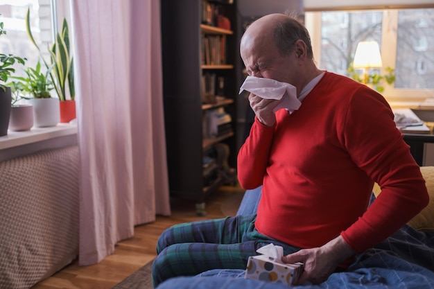 Senior man holding a tissue and sneezing sitting at home