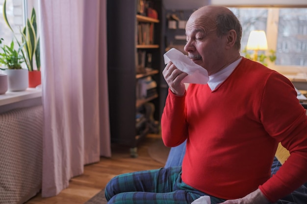 Senior man holding a tissue and sneezing sitting at home