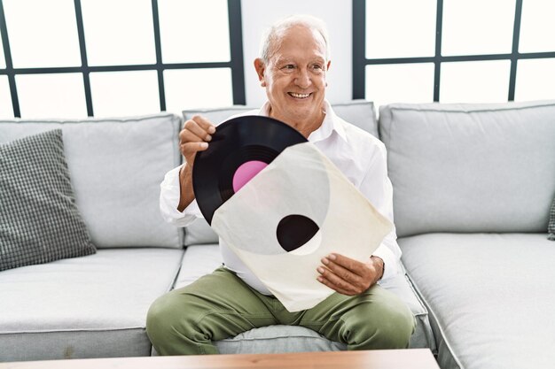 Старший мужчина держит виниловый диск, сидя дома на диване