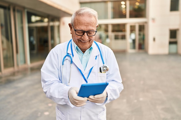 Senior man in doktersuniform met behulp van touchpad op straat