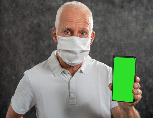 Senior man in een medisch masker met smartphone met groen scherm