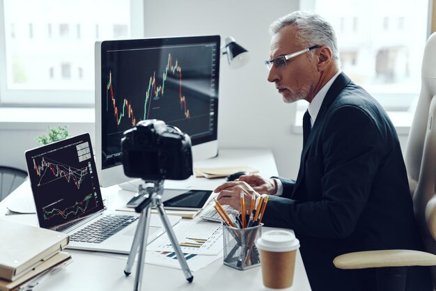 Senior man in elegant pak met behulp van moderne technologieën tijdens het maken van video's voor sociale media