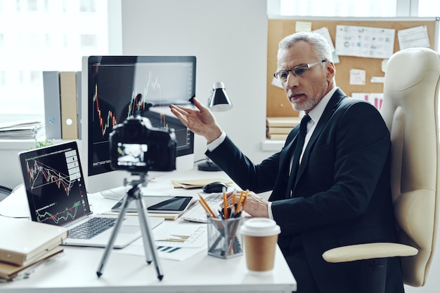 Senior man in elegant pak met behulp van moderne technologieën tijdens het maken van video's voor sociale media