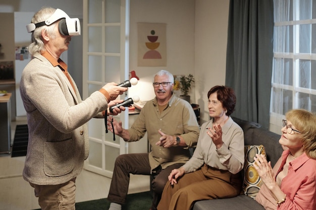 Senior man in vr-headset met gamepads terwijl hij het beeld op het scherm bestuurt