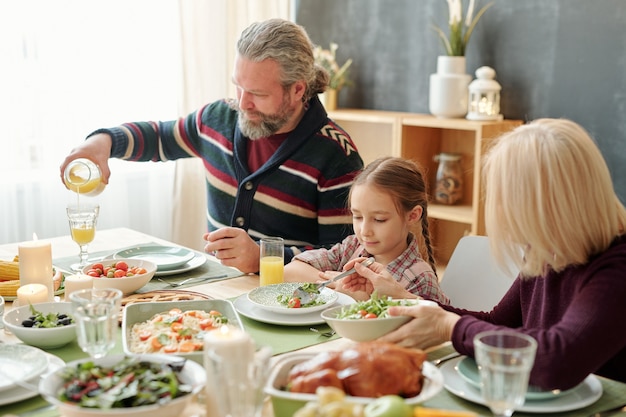 Senior man jus d'orange gieten in glas door feestelijke tafel tijdens familiediner met zijn vrouw en schattige kleindochter