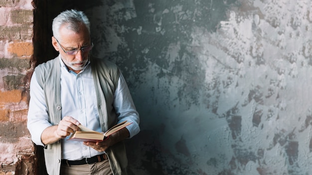 Фото Старший человек, склоняется к книге чтения кирпичной стены