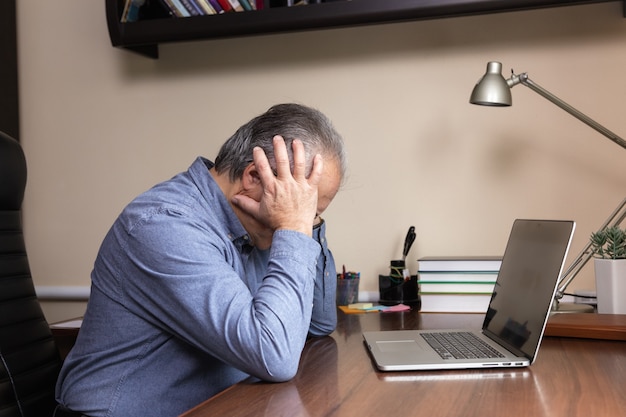 Senior man learn to use computer. Old man in glass and blue shirt using a laptop computer for online studying at home office