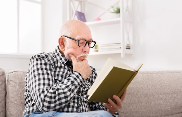 Senior man leest boek zittend op de bank thuis, kopieer ruimte