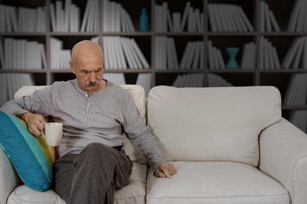 Senior man leest in een digitale tablet zittend op de bank in de huiskamer