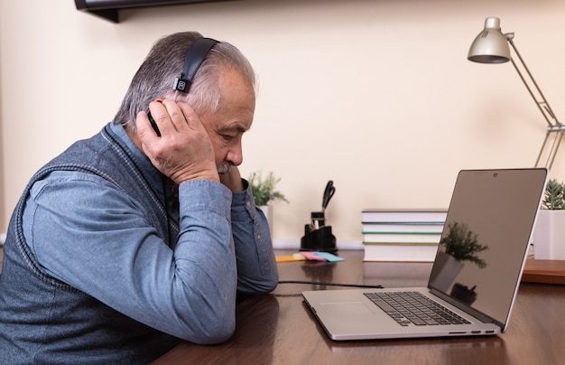 Senior man listening music. Happy elderly man wearing headphones at home with laptop. The concept of active old age