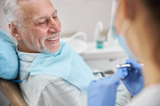 пожилой мужчина выглядит позитивно во время стоматологического осмотра в клинике