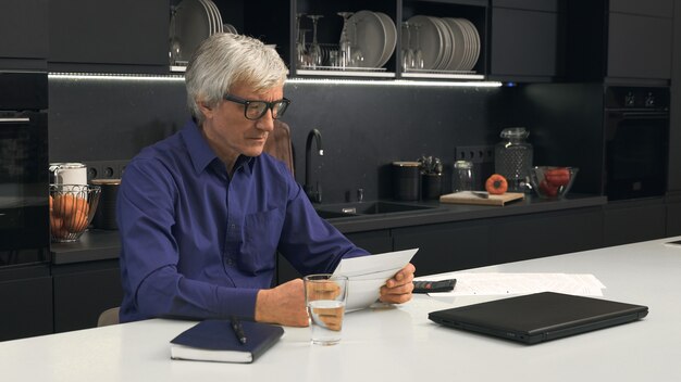 Senior man looks at closed letters in the kitchen