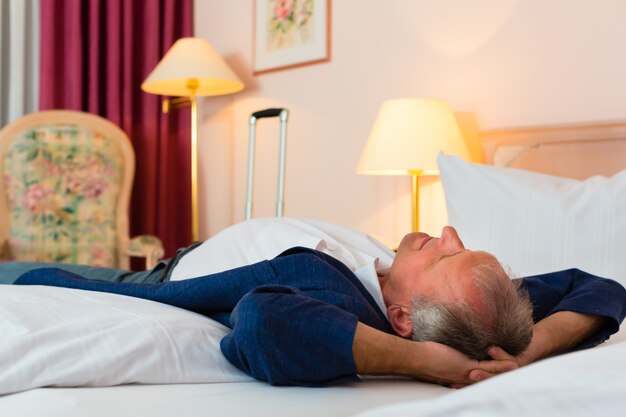 Senior man lying on the bed in the hotel room