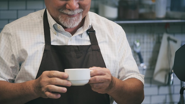 シニア男性はカウンターテーブルの後にコーヒーを作りますビジネスマンはコーヒーマシンを使用してコーヒーを作ります