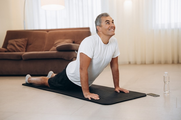 Senior man mediteert terwijl hij cobra pose doet in de woonkamer