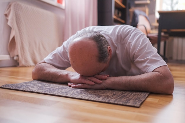 Senior man mediterend op een houten vloer en liggend in Shavasana pose