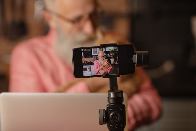 Foto senior man met baard maakt een blog, een volwassen man speelt met een kat.