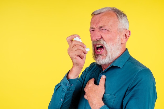 Senior man met behulp van een astma-inhalator in studio gele achtergrond.