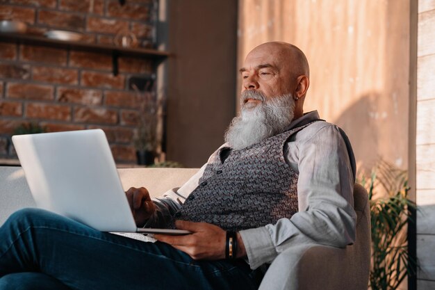 Senior man met een glas wijn met behulp van zijn laptop