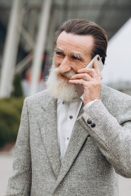 Senior man met een grijze baard en snor in een jas praat over de telefoon