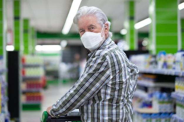 Senior man met ffp2-masker om besmetting door covid 19 coronavirus te voorkomen die kar in supermarkt duwt