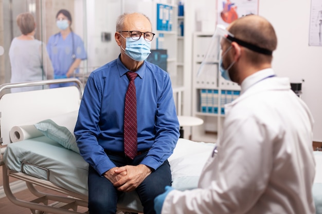 Senior man met gezichtsmasker als veiligheidsmaatregel luisterende arts diagnose in de loop van covid19