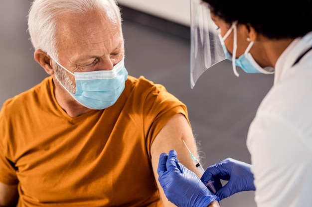 Senior man met gezichtsmasker tijdens het ontvangen van vaccin in de medische kliniek